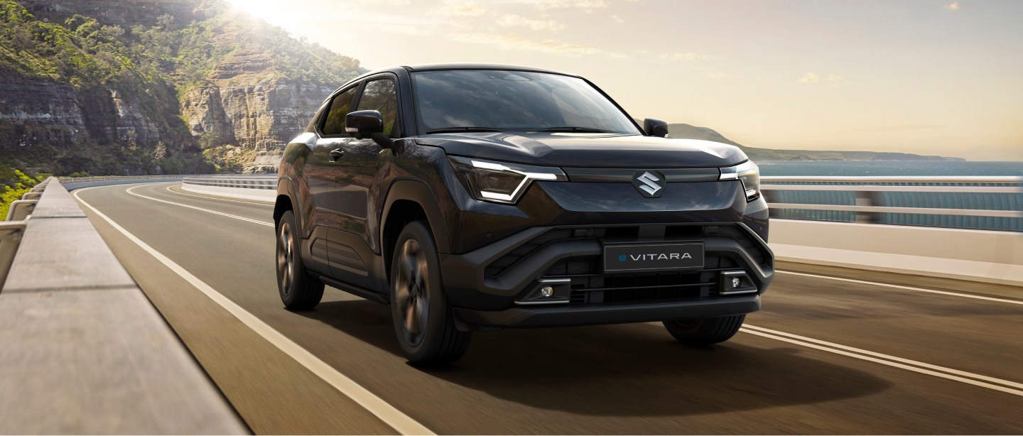 Schwarzer Suzuki e Vitara fährt auf einer Küstenstraße bei Sonnenschein Schwarzer Suzuki e Vitara fährt auf einer Küstenstraße bei Sonnenschein