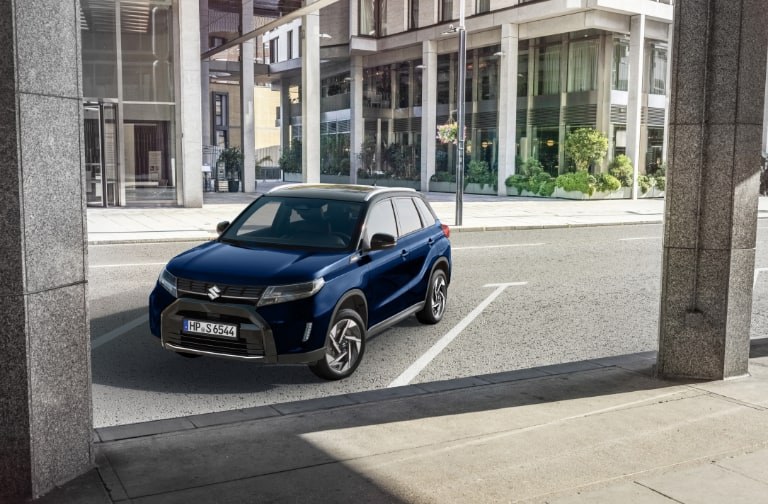 vitara-alarmanlage.jpg Suzuki Vitara Hybrid in Solar Yellow Pearl Metallic, Mann in dunkelblauem Anzug daneben, welcher gerade den Schlüssel bedient.