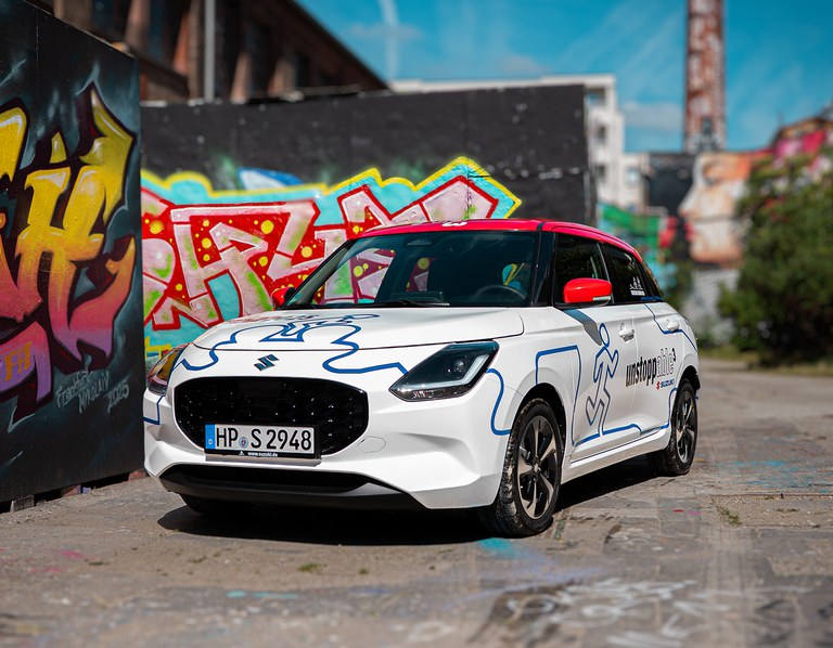 swift-triathlon-gewinnspiel-2025-q3.jpg Der Suzuki Swift im unstoppable Look vor einer Wand mit Graffiti.