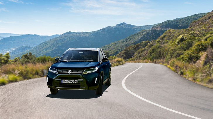 Ein Suzuki Vitara Hybrid in Blue Sphere Pearl Metallic auf einer leeren Fähre, von oben fotografiert. Eine Frau steigt ein.